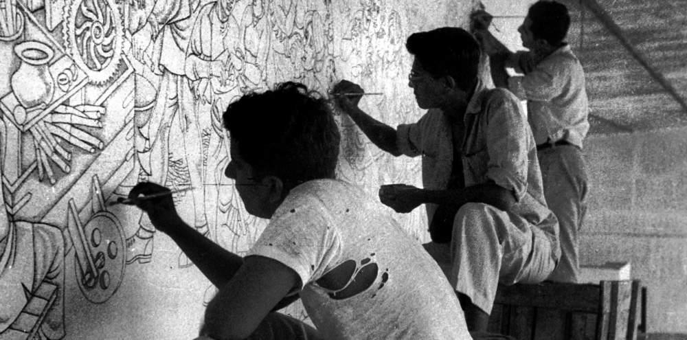 Three students paint different sections of a wall mural.