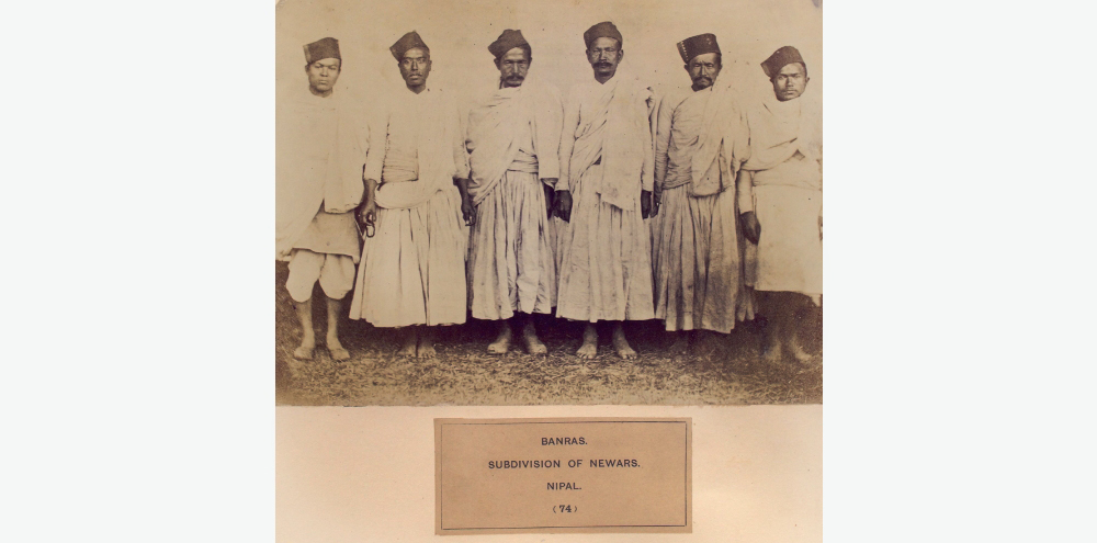 Six men wearing long shirts, loose trousers and caps stand shoulder to shoulder as they pose for the camera.