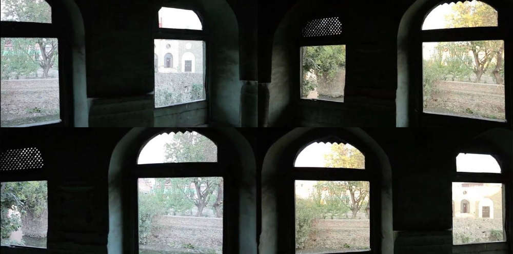 A narrow film still with two rows of arched windows facing towards the trees and buildings outside.