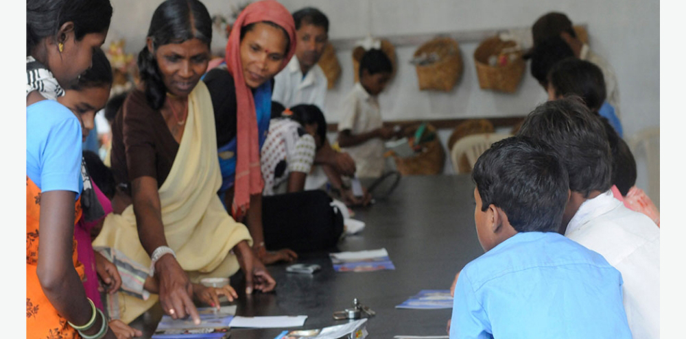 A group of women and children are sitting and engaging in conversation around a table.