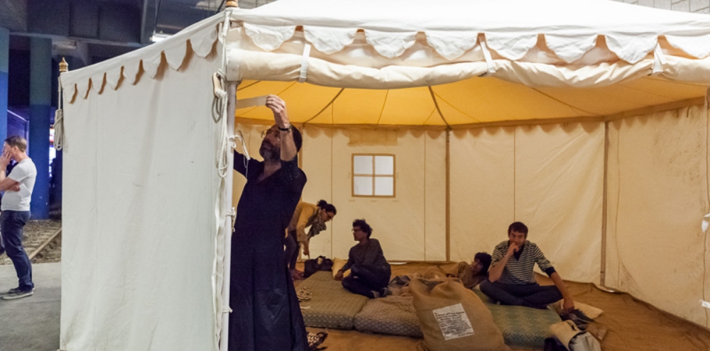 A man taping the interior of a tent while four individuals lie on the futon behind him.