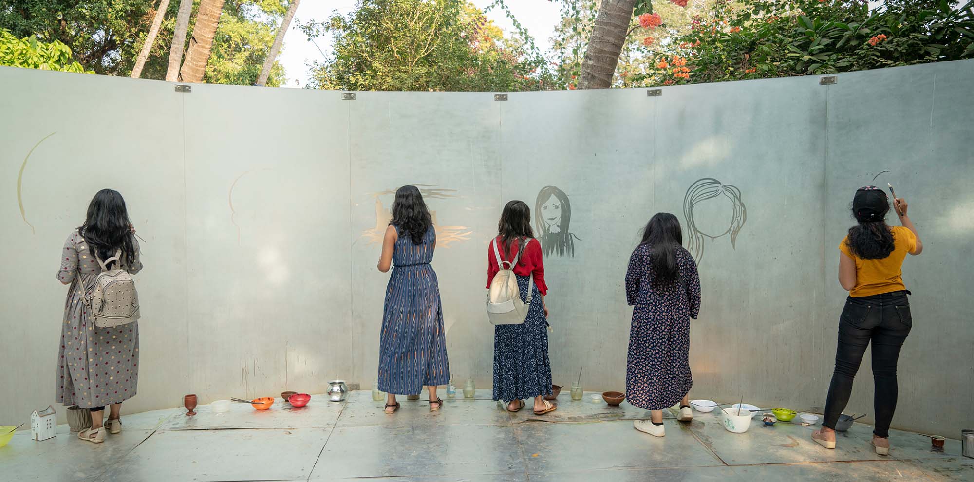 Many women draw their faces on a fogged-up curved glass structure with their backs facing us.