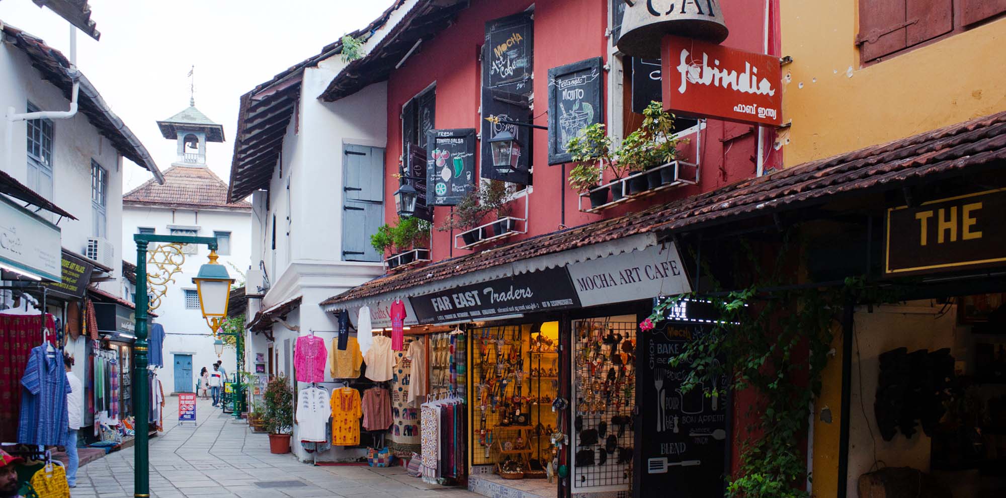 A shopping street with various stores on either side and a bell clock tower visible in the background.