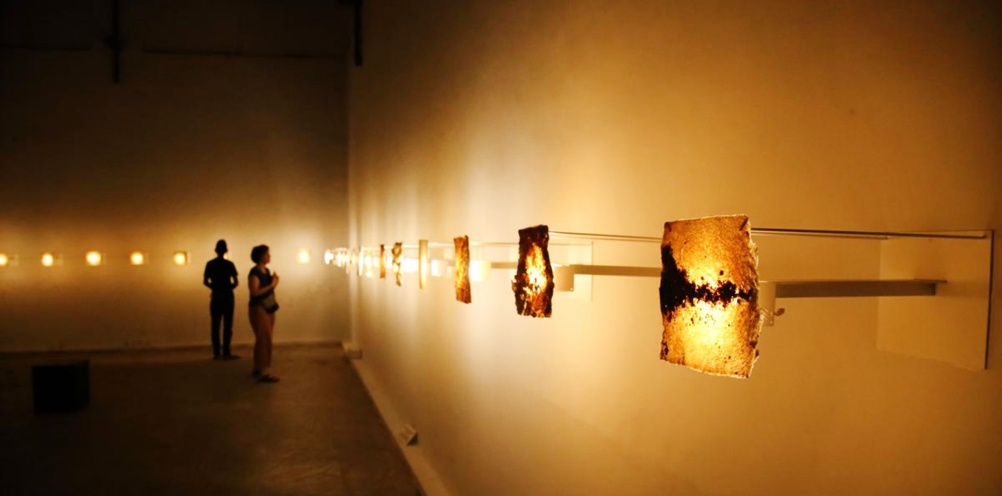 Two people admire several organic papers lit up by yellow bulbs at the back.