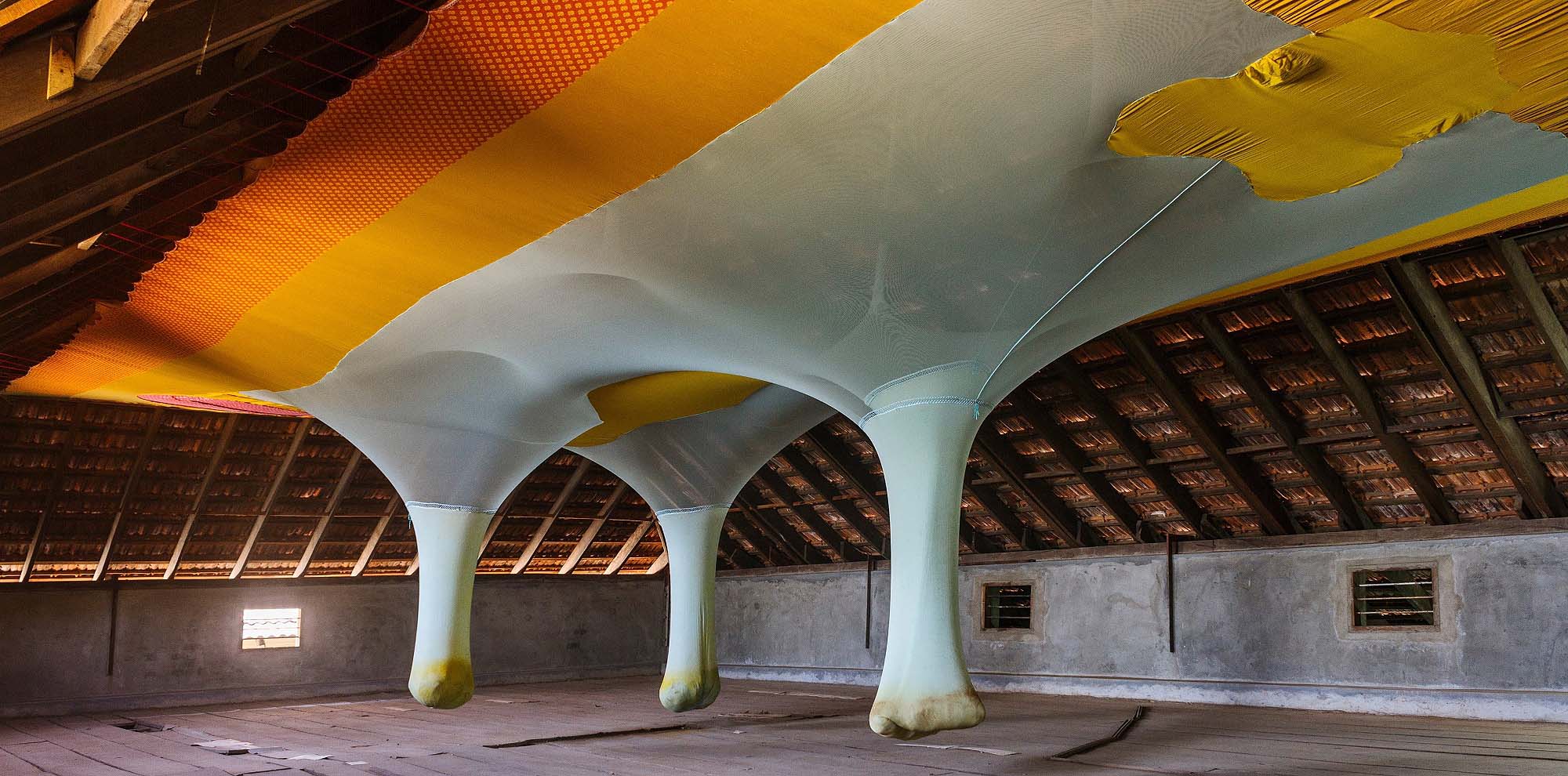 An installation of stretched cloth over the sloped ceiling with three weighed-down pockets full of unidentifiable objects.