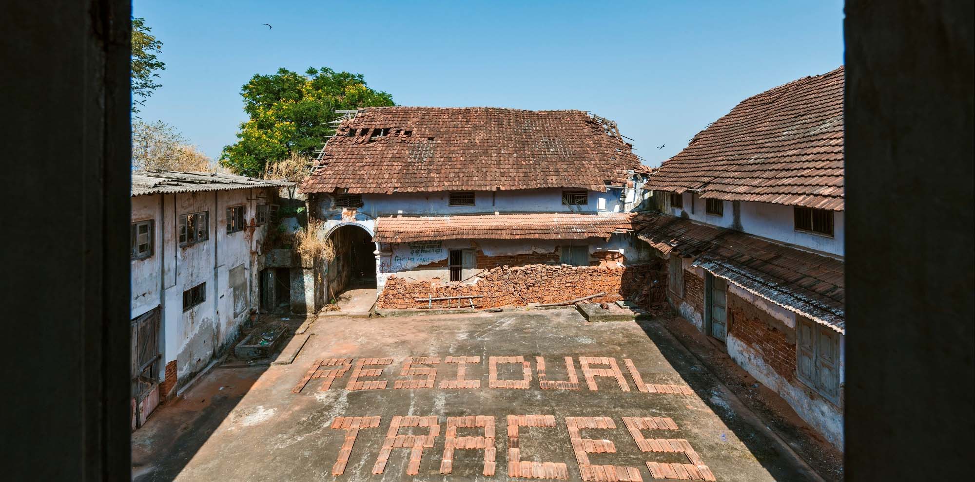 An open courtyard of an abandoned building with the English text ‘Residual Traces’ written with bricks in the centre.