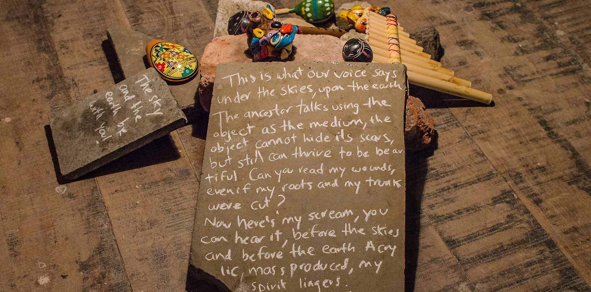 Two flat rocks with text written in chalk propped up on the floor among several multi-coloured wooden toys.