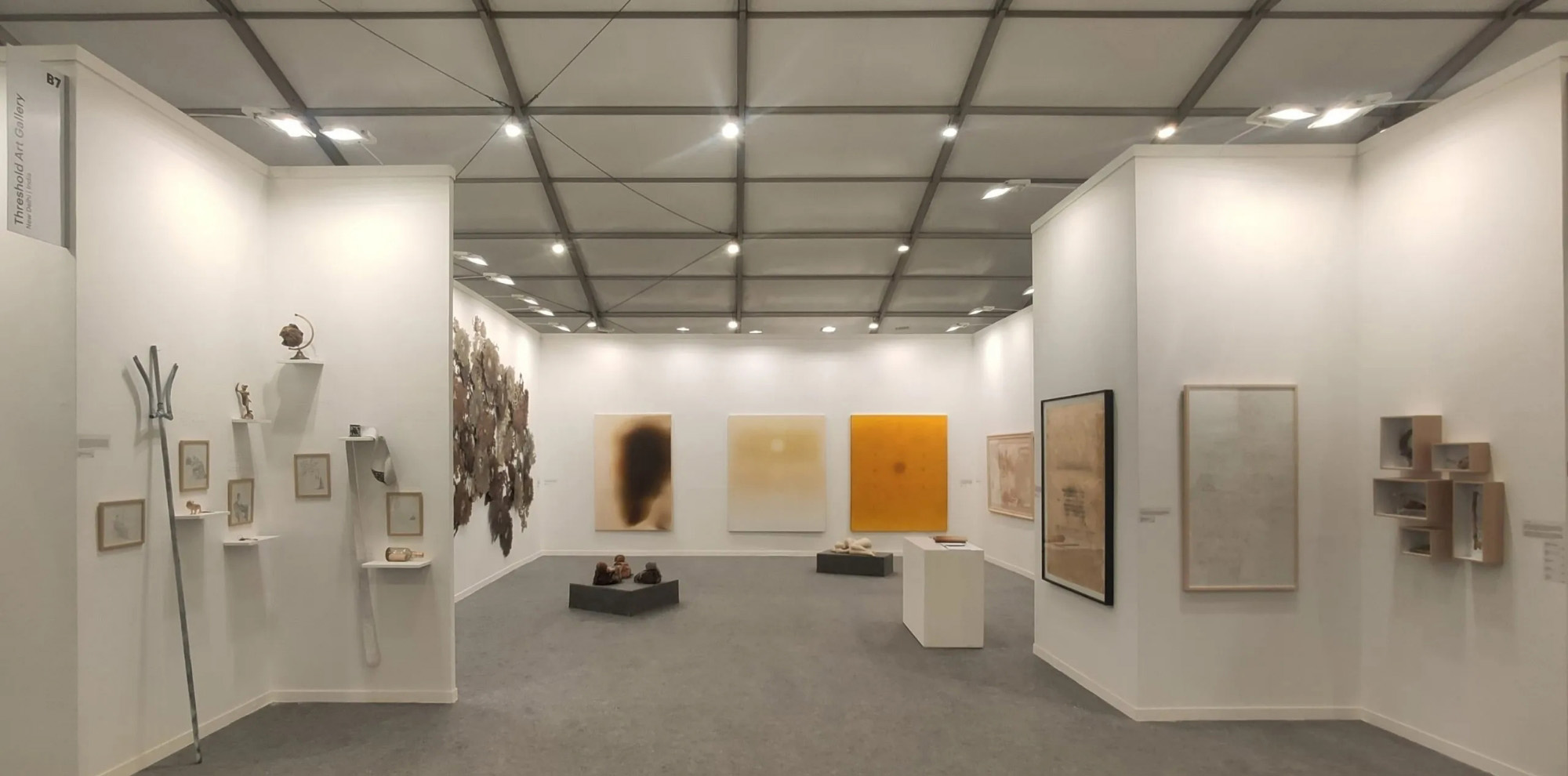 Several framed artworks and sculptures on pedestals are displayed on the walls of an exhibition space.