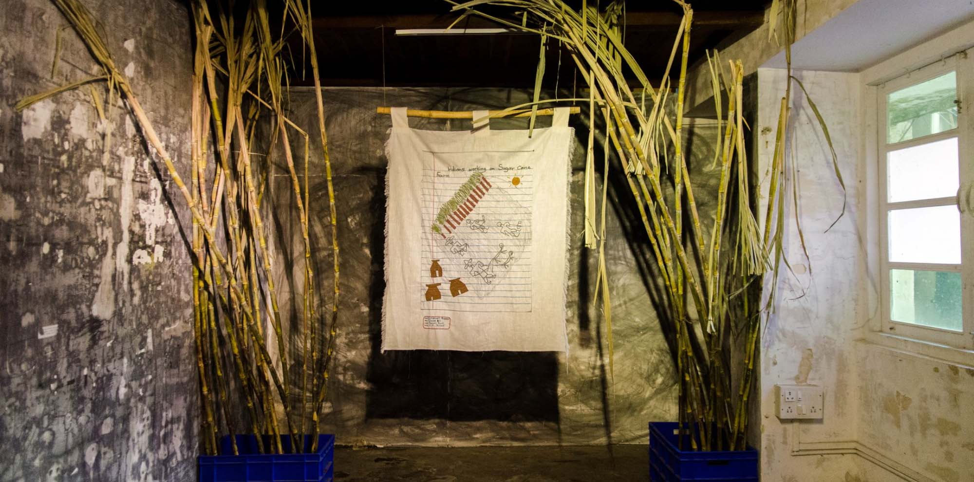 A hanging cloth with illustrations flanked by bamboo shoots in front of grey walls.