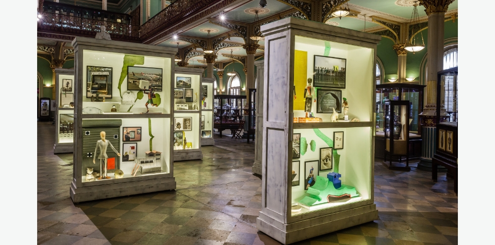 Tall glass cabinets filled with various photographs and figurines in an exhibition hall.