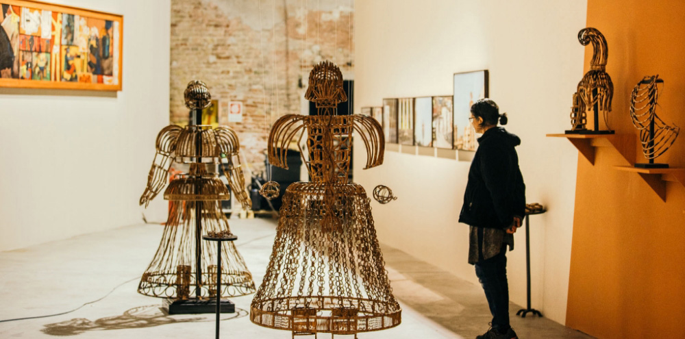 An exhibition space with metal wire framework sculptures and framed displays in the background.