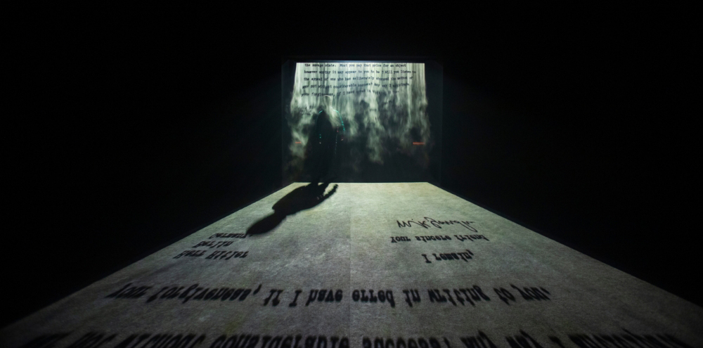 A dark room with textual projections on a fog screen and floor.