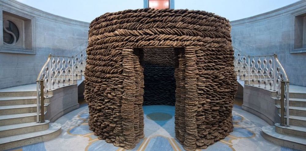 A cylindrical structure with a doorway is created using stacked cowpats installed in front of a double staircase.