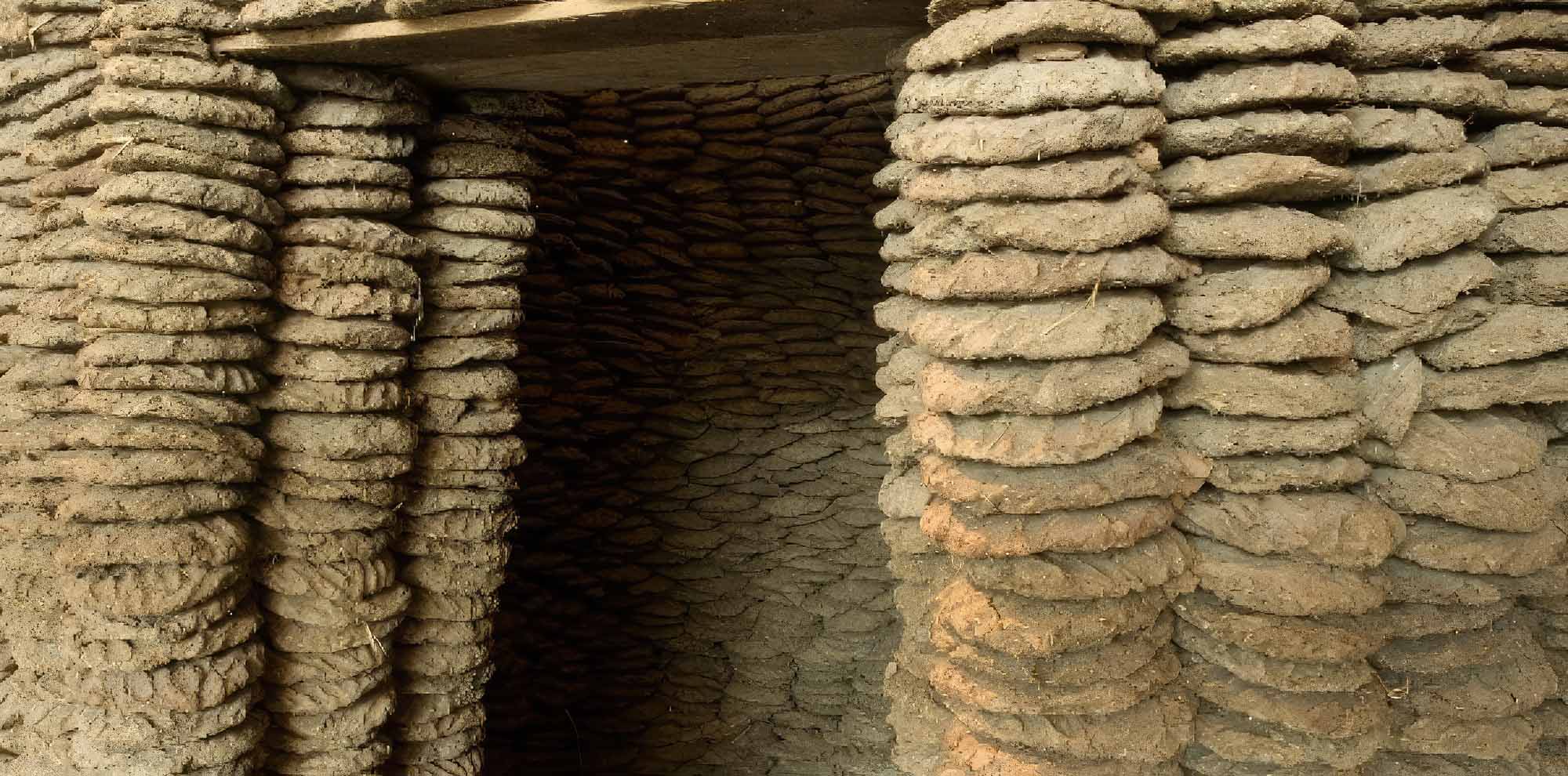 A close-up photograph of a circular structure with a doorway created using layered cowpats.